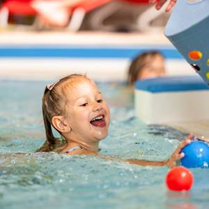 Mädchen sammelt Bälle im Wasser ein.
