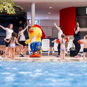 Kinder, Betreuer und Maskottchen HopiHo tanzen am Rand des Indoorpools.