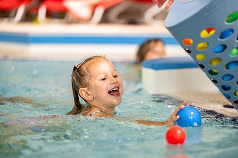 Mädchen sammelt Bälle im Wasser ein.